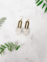 Load image into Gallery viewer, speckled white and grey leather earrings with a brass horseshoe accent
